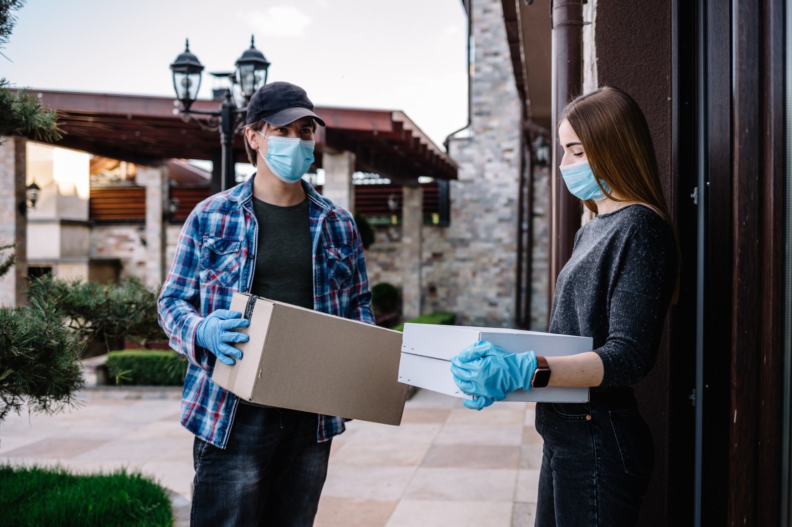 Woman receiving parcel from delivery man at the door. medical mask, quarantine